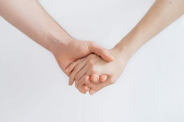 Two hands are clasped together, showing a gesture of support and solidarity. The background is plain white, emphasizing the connection and care between the individuals.