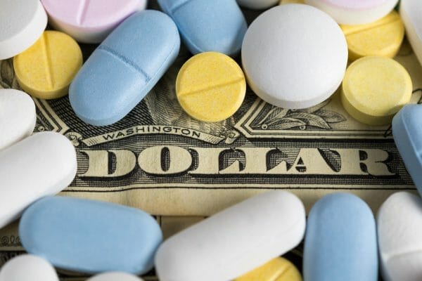 Various colorful pills and tablets are scattered over a U.S. dollar bill. This image represents the high cost of medication and financial challenges associated with medical treatment.