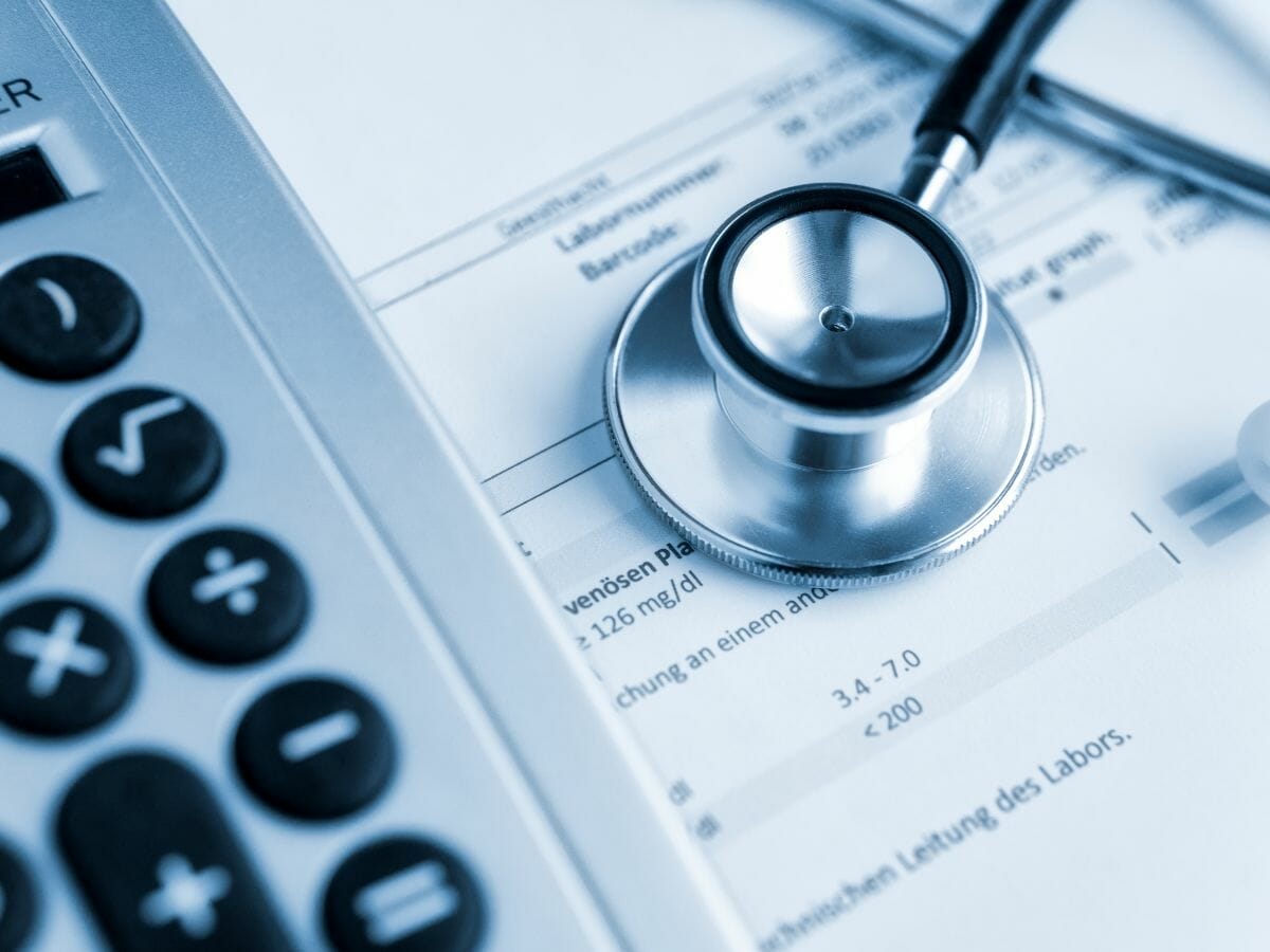 A stethoscope and a calculator lie on top of medical bills and documents, symbolizing the financial challenges of healthcare and medical expenses.