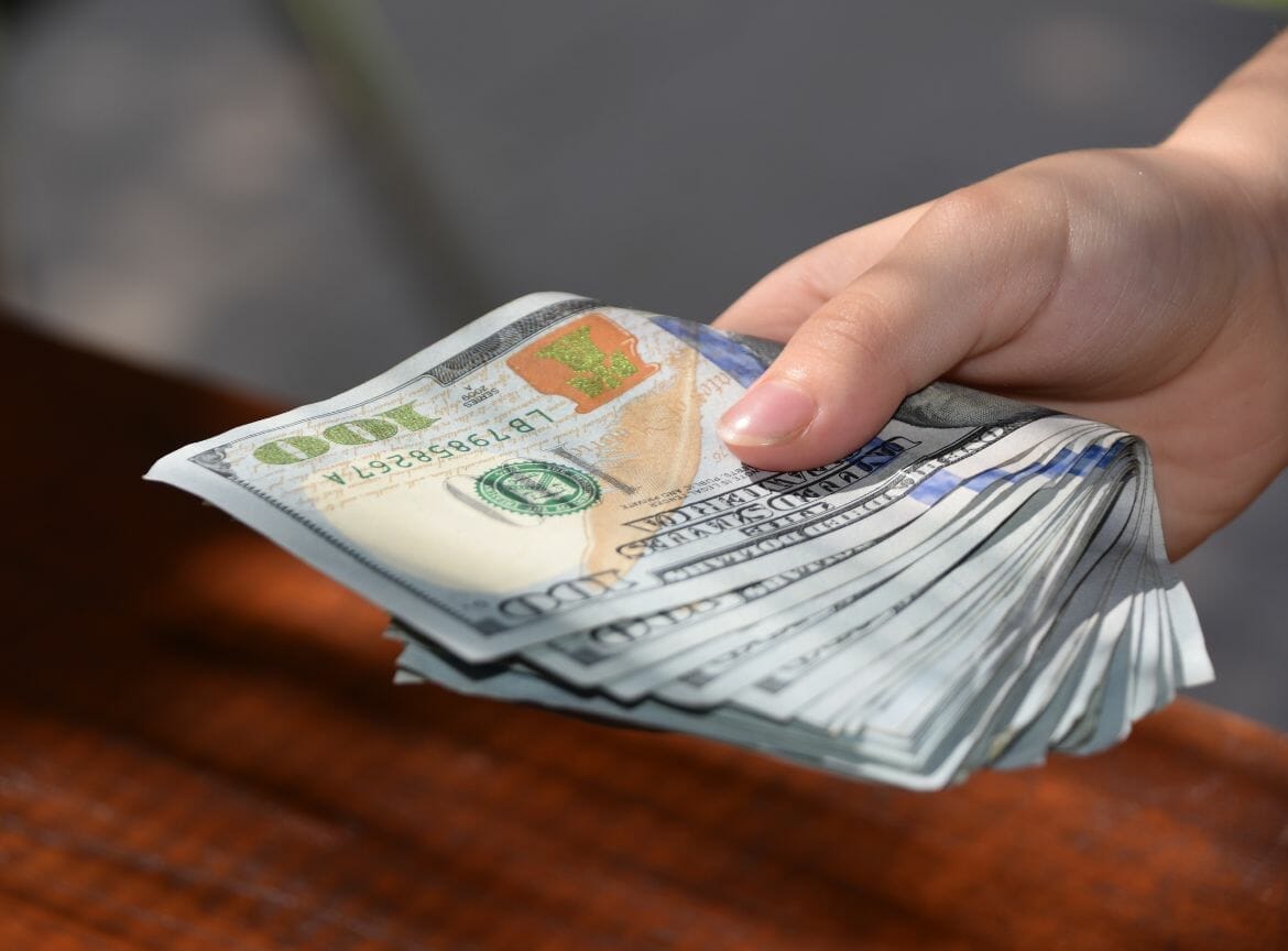 Hand holding a stack of hundred-dollar bills, representing financial assistance for sarcoma cancer patients.