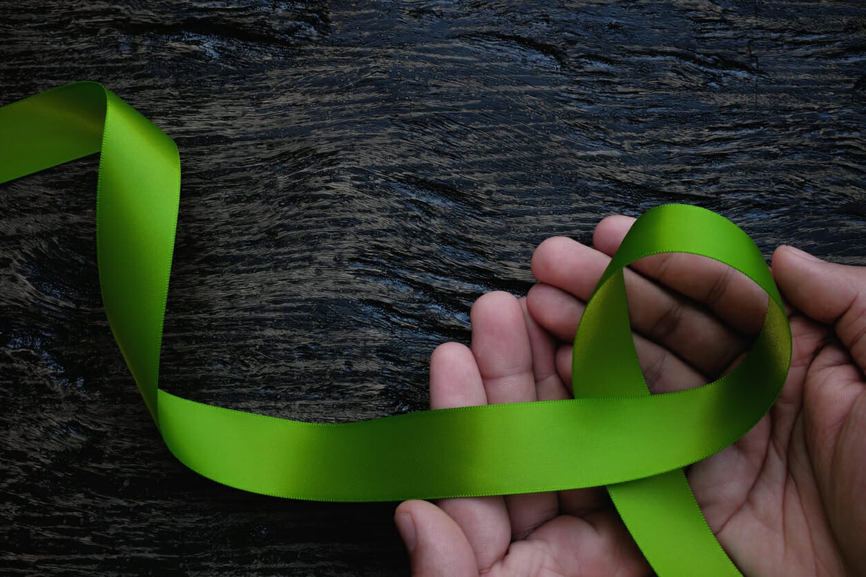 Hands holding a green awareness ribbon, symbolizing financial assistance for Non-Hodgkin's Lymphoma patients.