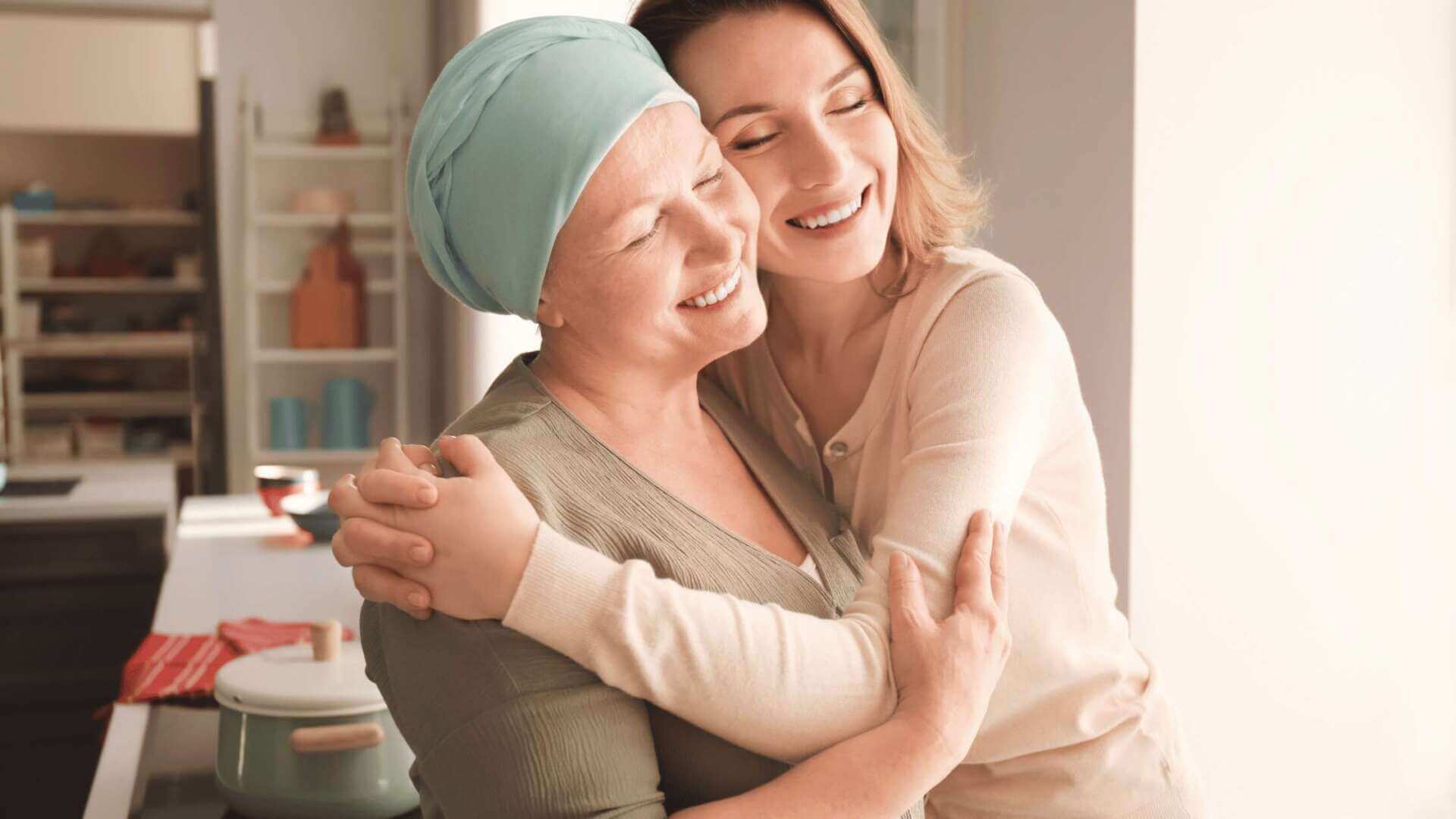 Smiling woman in a blue headscarf embracing her caregiver in a kitchen, highlighting support in viatical settlements